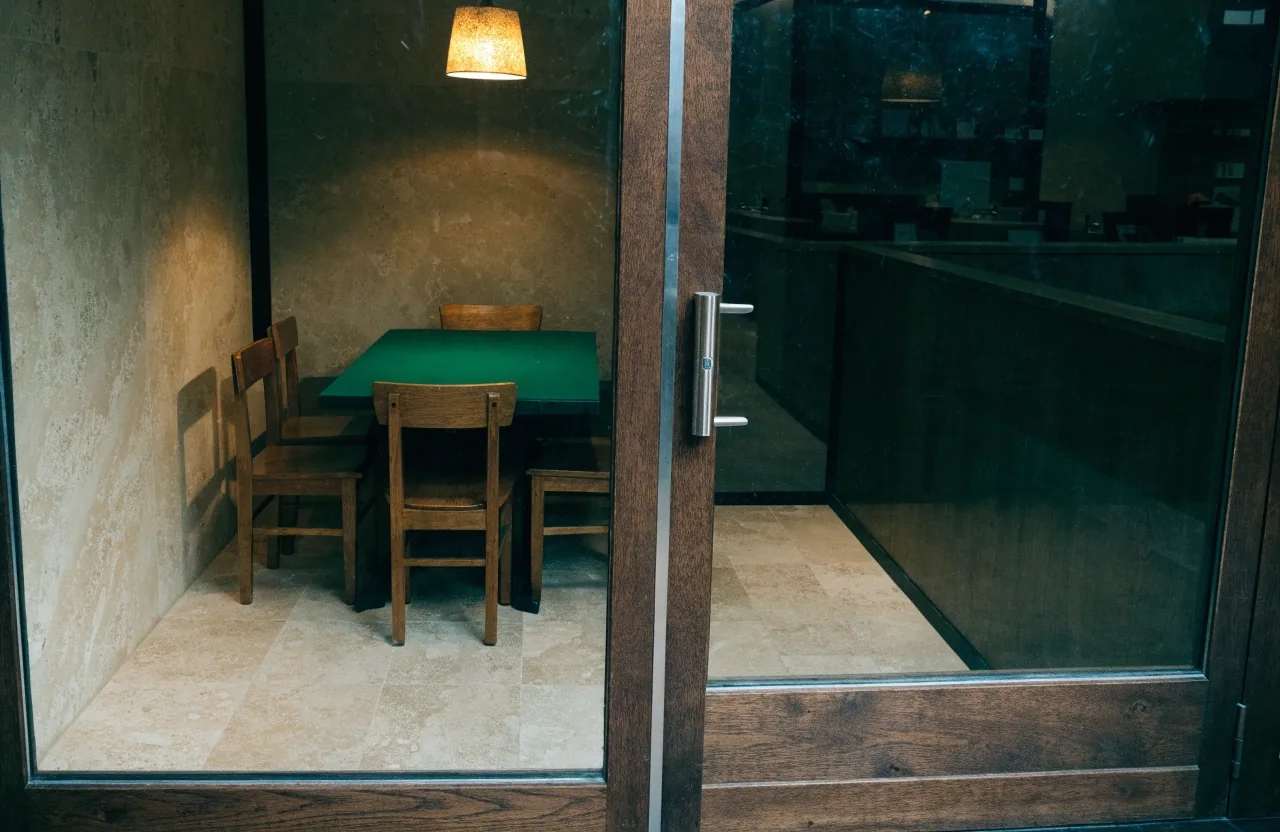 Pohled skrz sklo do odděleného pokerového salonku před otevřením, rozsvícené pendantní světlo nad stolem